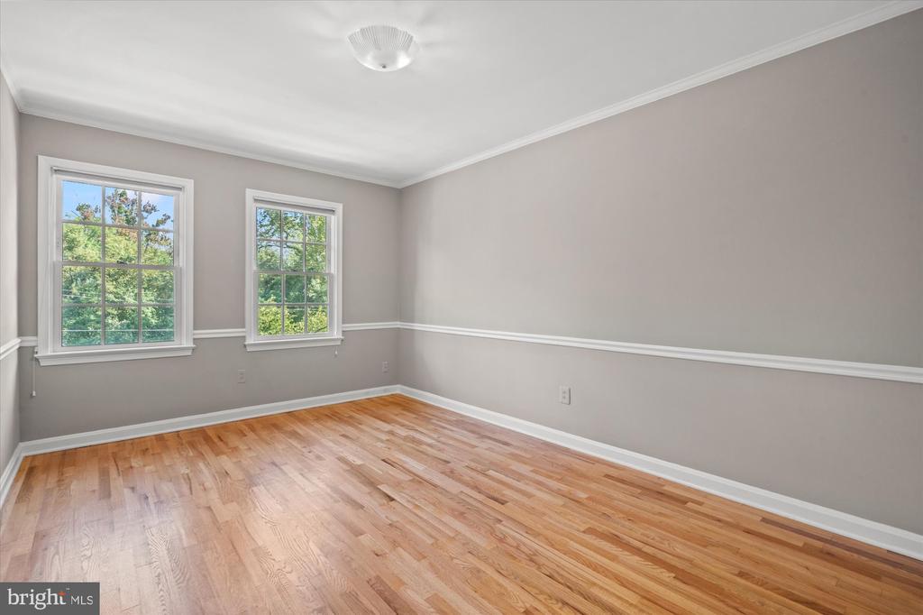 Empty room with hardwood floors, gray walls, and two windows overlooking trees.