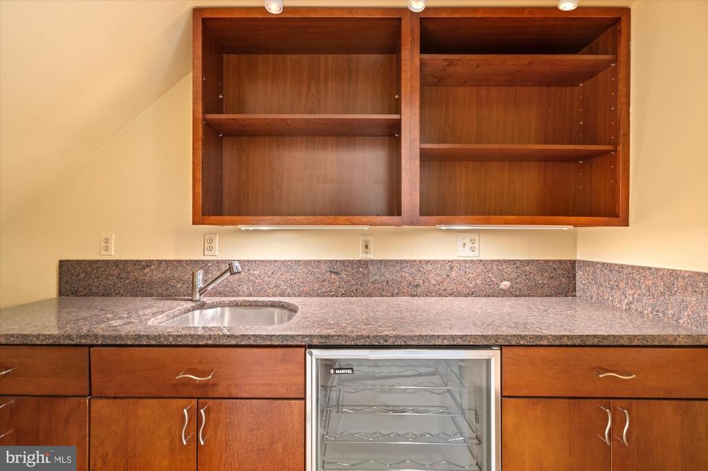 Kitchen counter with a sink, granite backsplash, wooden cabinets, and an under-counter beverage refrigerator.