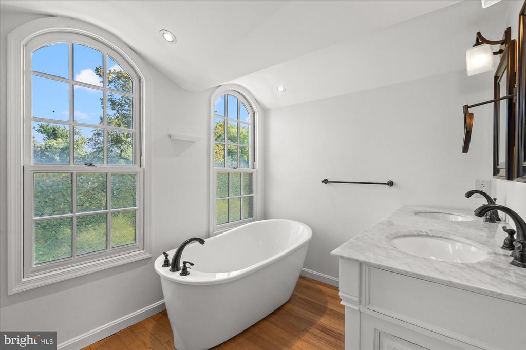 Bathroom with a freestanding soaking tub beneath arched windows and a marble double vanity.