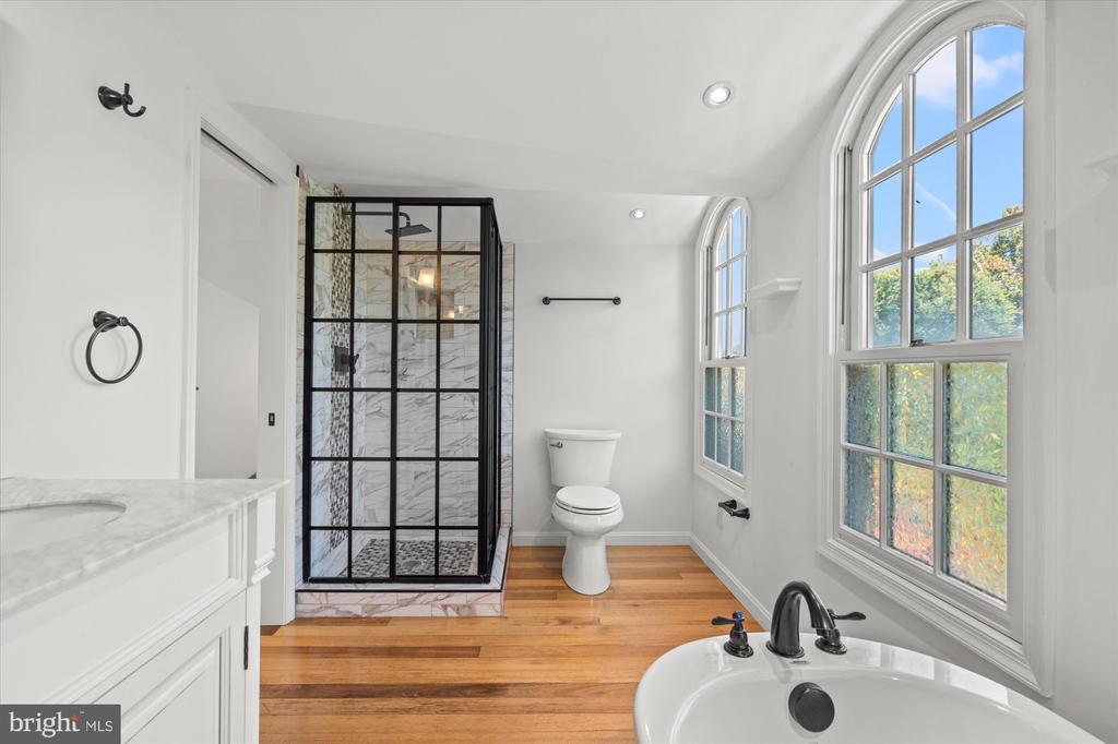 Bathroom with a freestanding tub, arched windows, and a black-framed marble-look shower.