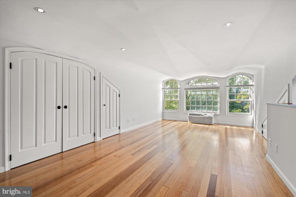 Vacant room with hardwood floors, paneled closets, and three arched windows.