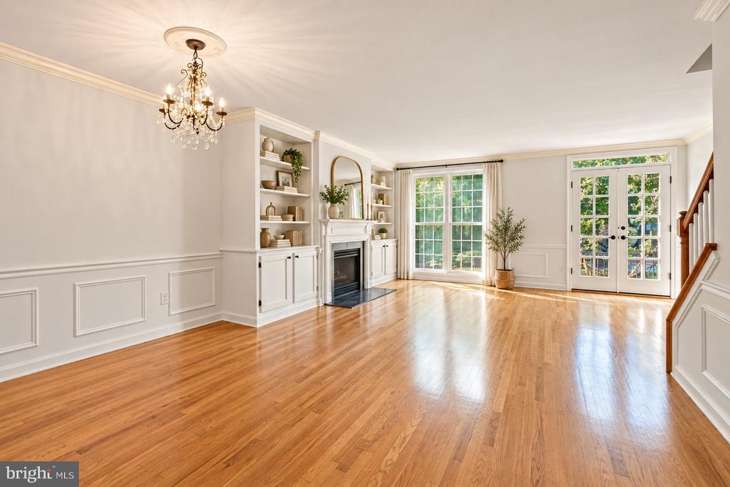 Vacant living room with hardwood floors, built-in shelving, a fireplace, and French doors to the yard.