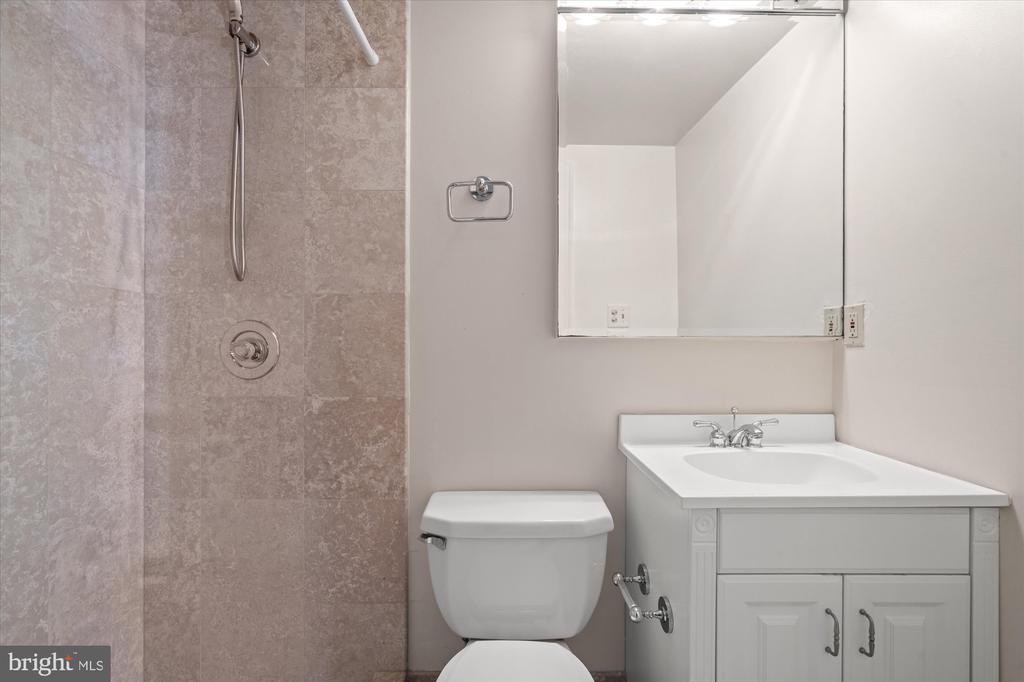 Bathroom with a tiled shower, white vanity, toilet, and large mirror.