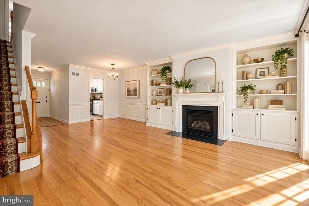 Living room with hardwood floors, white fireplace, built-in shelves, and staircase.