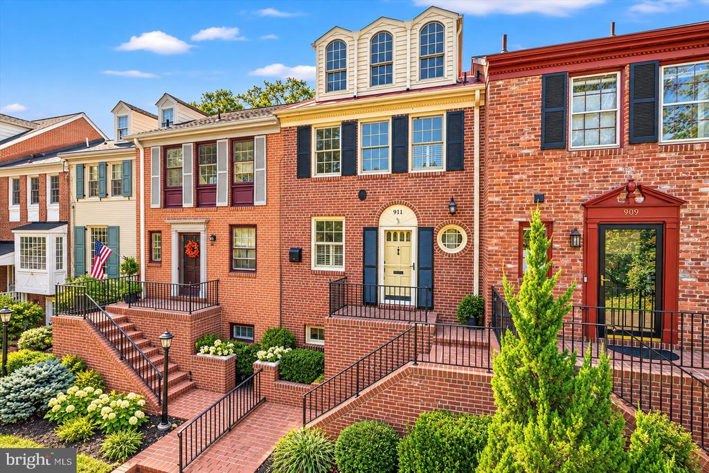 Red-brick townhouse with a three-window dormer, brick steps, and landscaped front garden.