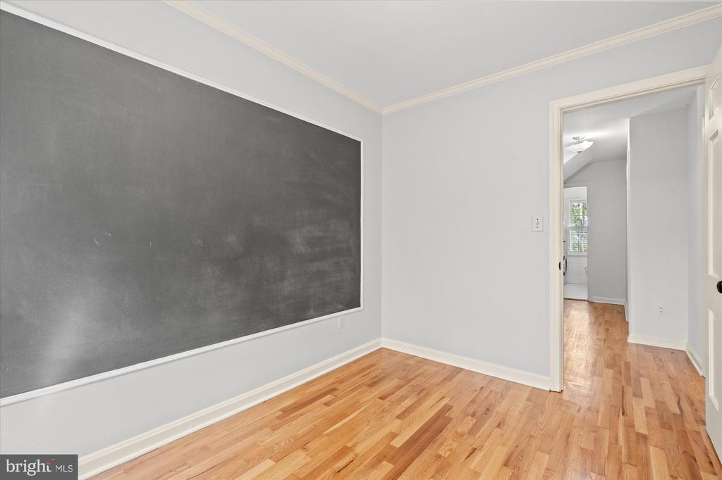 Empty room with a large chalkboard wall and hardwood floors, looking through an open doorway.