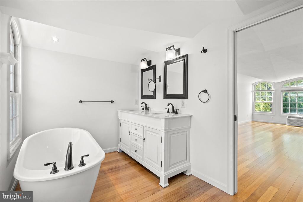 Bathroom with a freestanding soaking tub, double vanity, dark-framed mirrors, and warm wood floors.