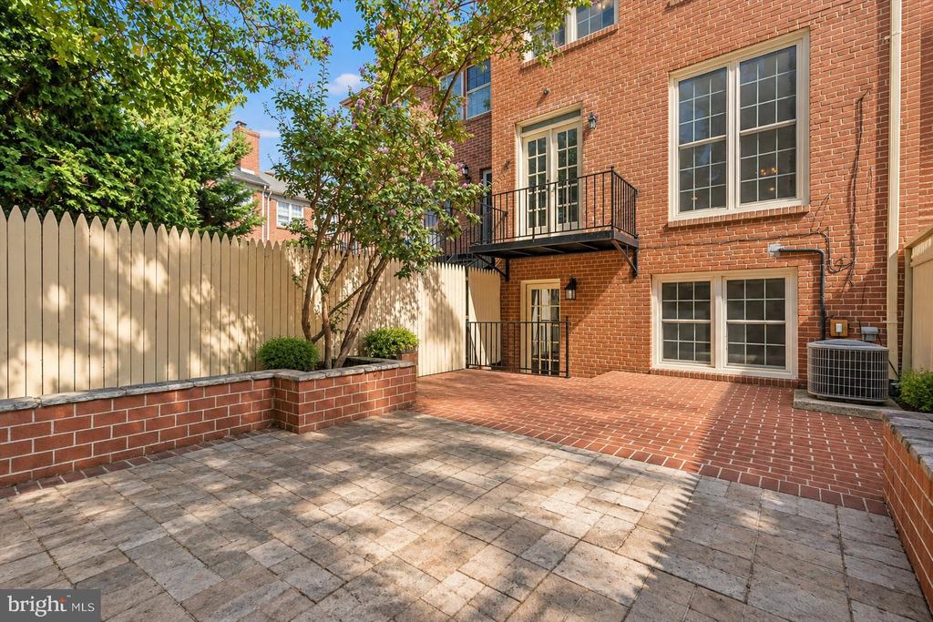 Brick townhouse courtyard with a raised balcony, paved patio, and leafy tree.