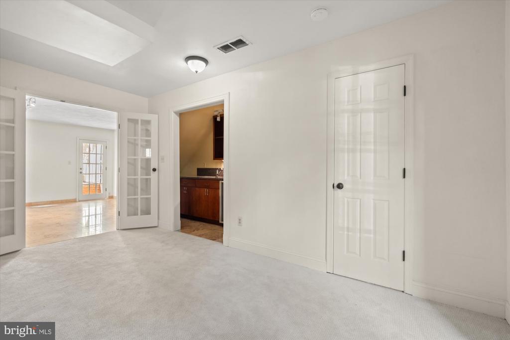 Carpeted room with French doors to a bright adjoining room and a doorway to the kitchen.