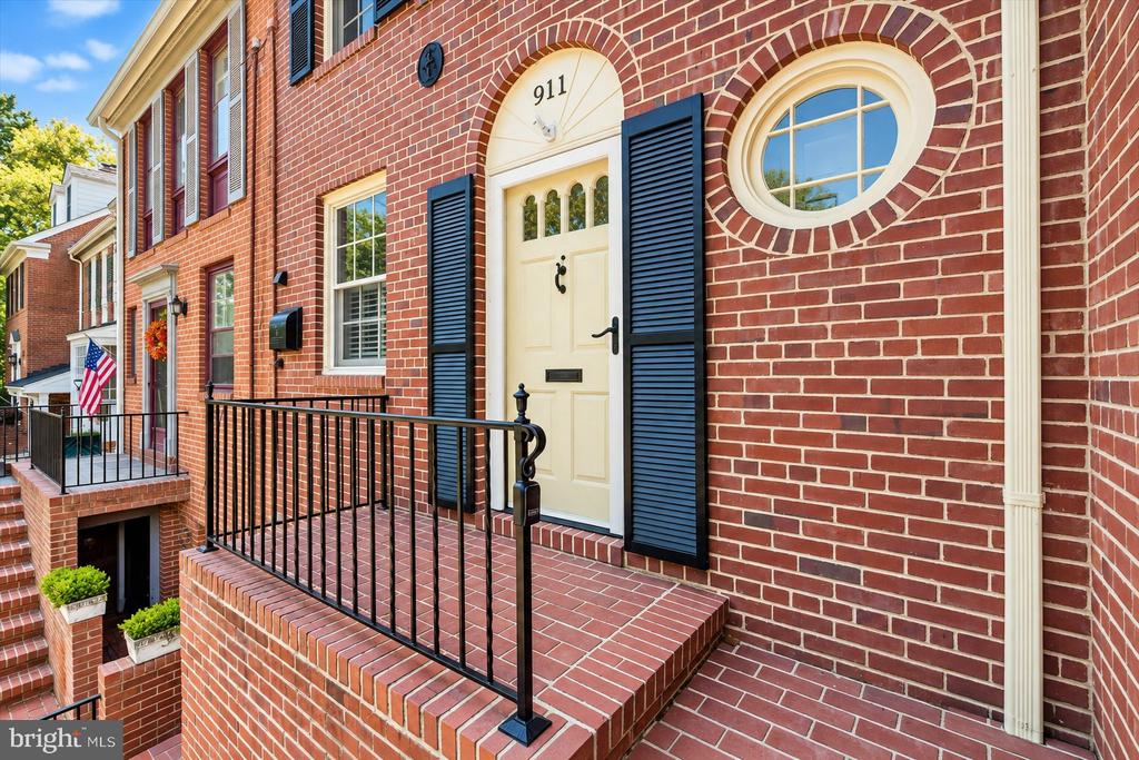 Red-brick townhouse entrance with an arched cream door, navy shutters, and a round window.
