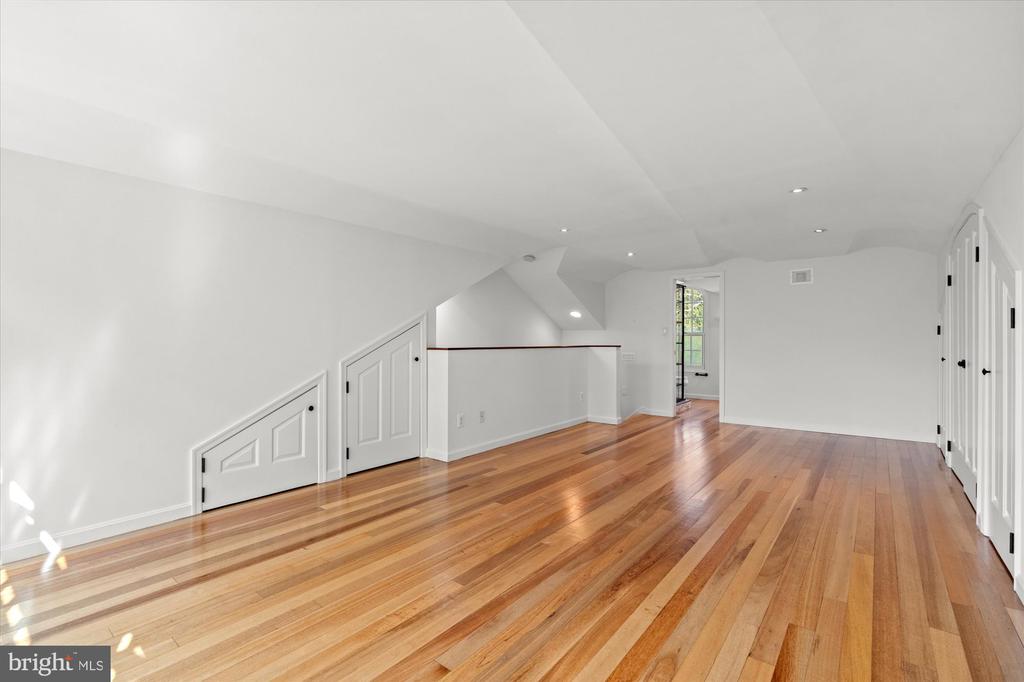 Empty upper-level room with hardwood floors, a sloped ceiling, and built-in storage beneath the eaves.