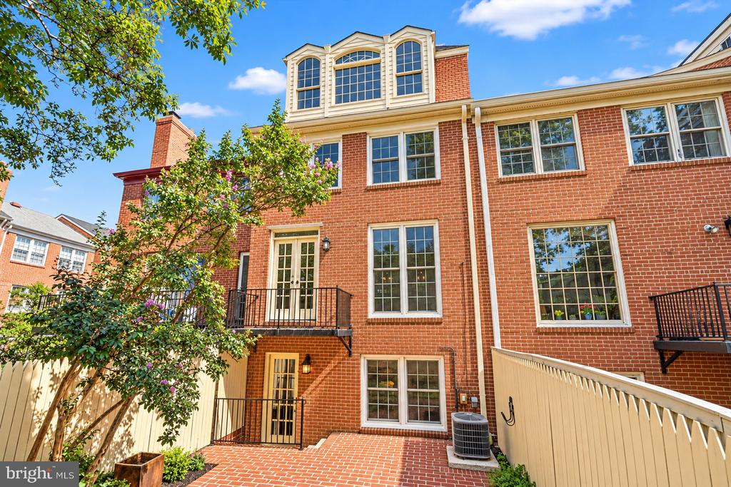 Red-brick townhouse rear exterior with balconies, a brick patio, and a leafy flowering tree.