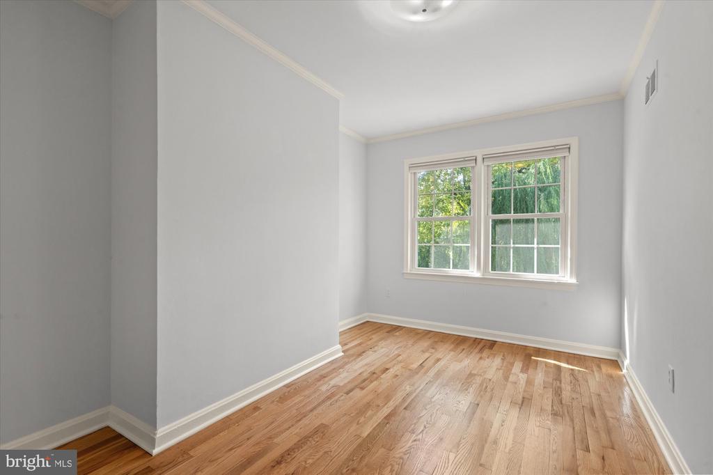 Vacant room with hardwood floors, gray walls, and two windows overlooking greenery.
