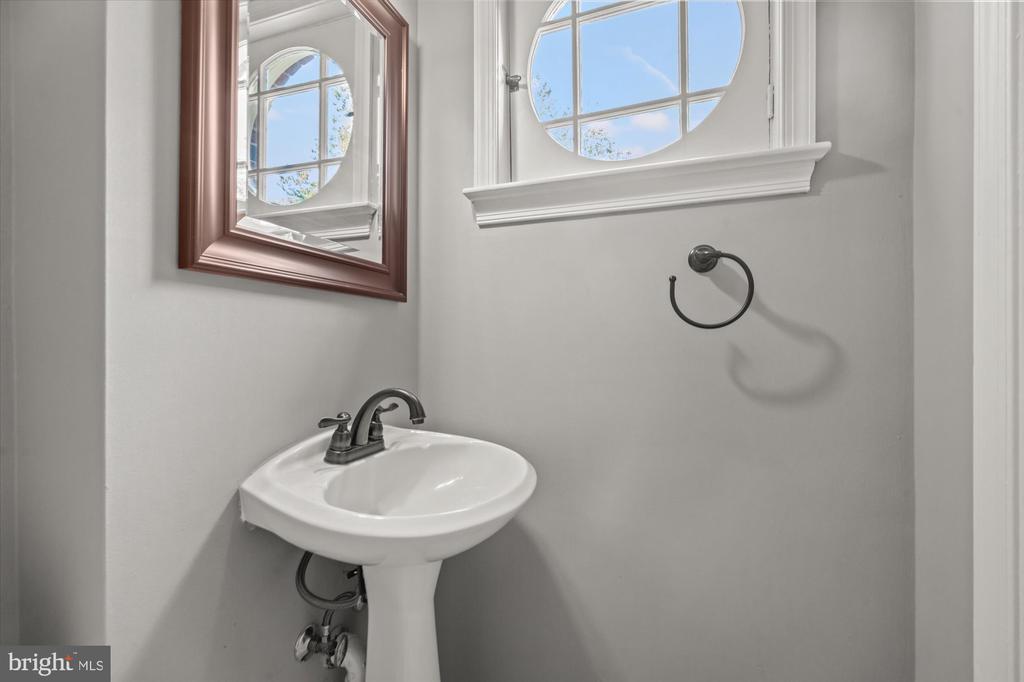 Bathroom with a white pedestal sink beneath a round-top window and wood-framed mirror.