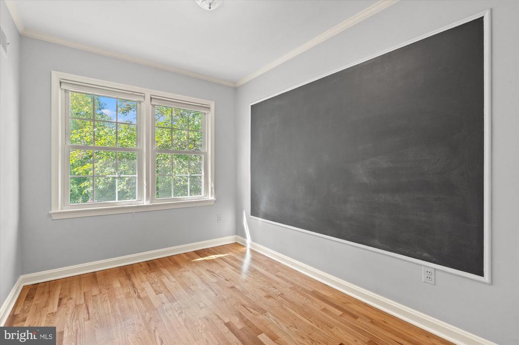 Empty room with hardwood floors, two windows, and a large chalkboard wall.