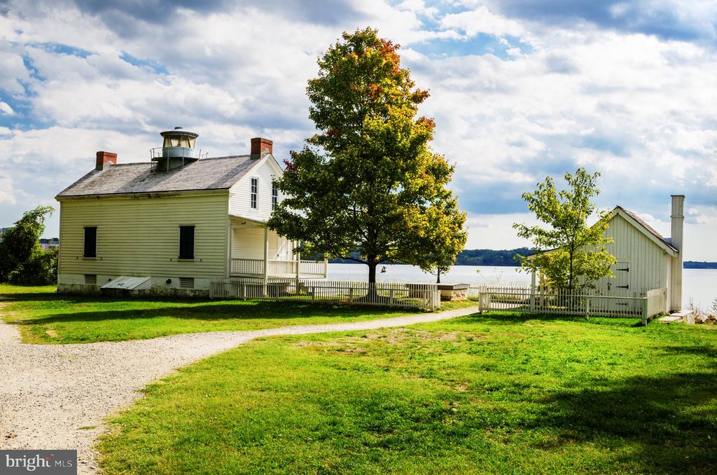 Pale clapboard house beside the water, with a gravel drive, large tree, and small outbuilding.