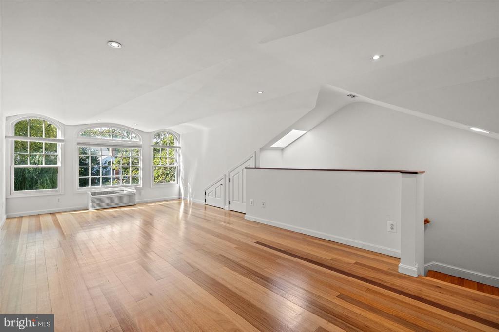 Vacant upper-level room with hardwood floors, arched windows, and a low partition.