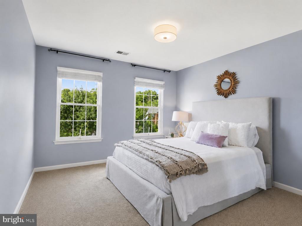 Bedroom with a white bed, upholstered headboard, two windows, and a gold sunburst mirror.