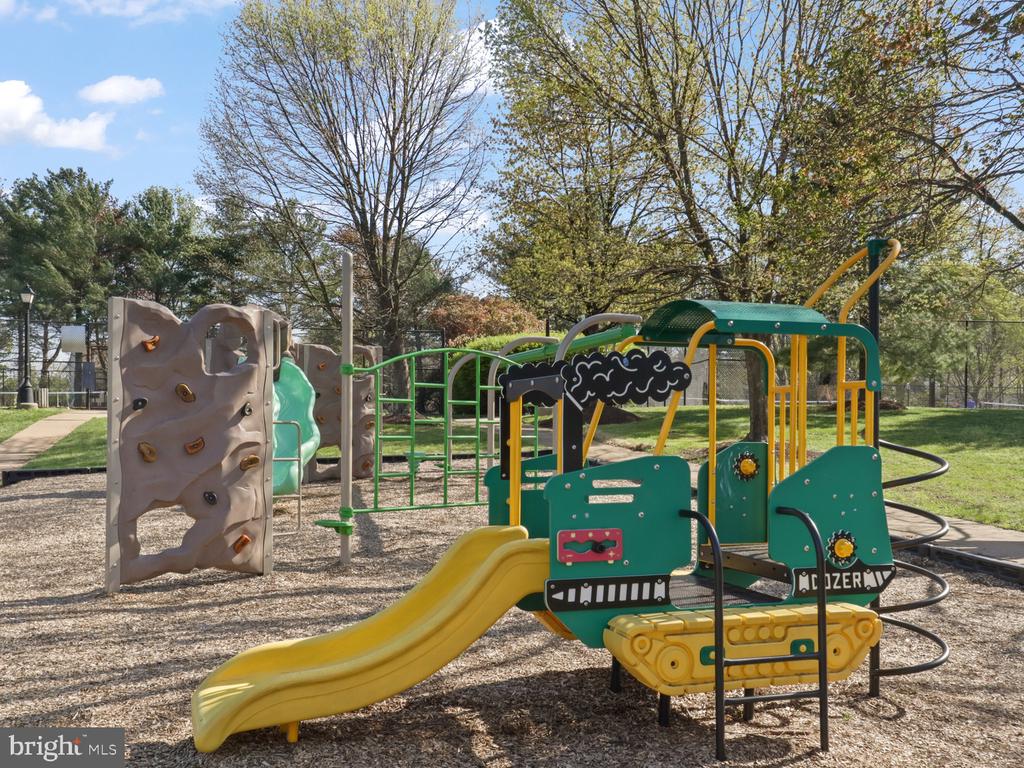 Community playground with a yellow slide and bulldozer-themed play structure beside a climbing wall.