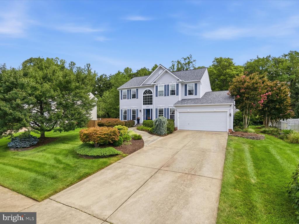 Two-story white house with an arched window, attached garage, landscaped lawn, and broad driveway.