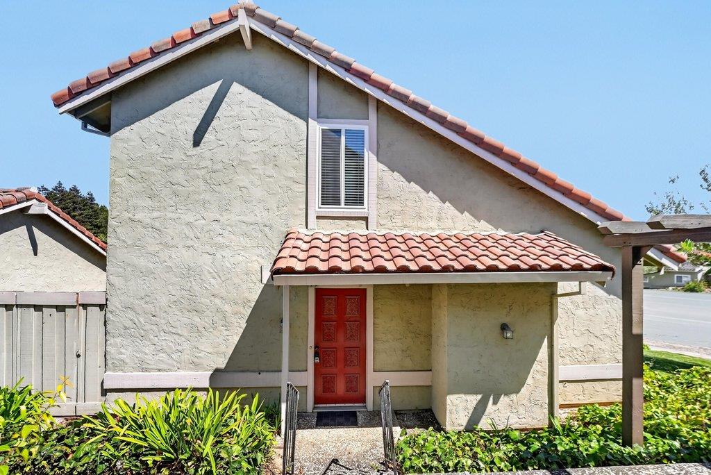 Stucco home with a terracotta tile roof, red front door, and landscaped entry walkway.