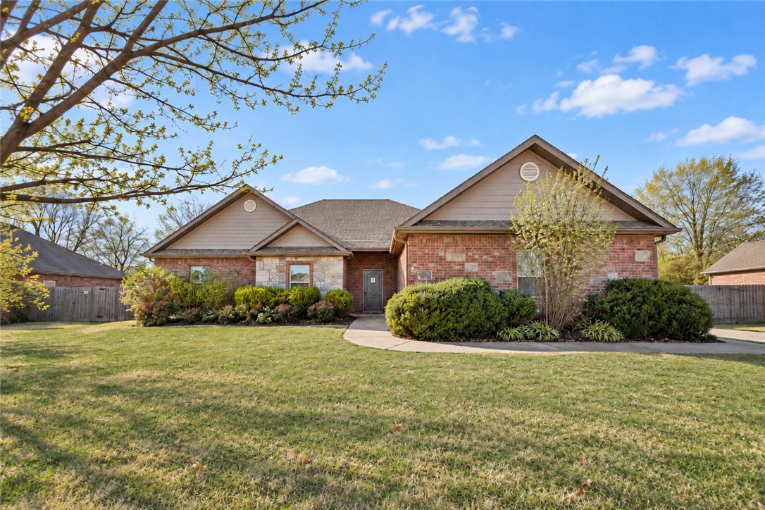 Brick house with tan gabled roofs, stone accents, landscaped shrubs, and a broad front lawn.