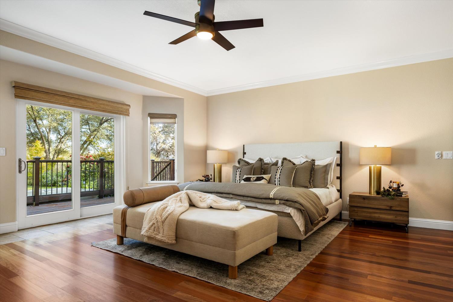 Primary bedroom with a king bed, chaise, hardwood floors, and glass doors opening onto a deck.