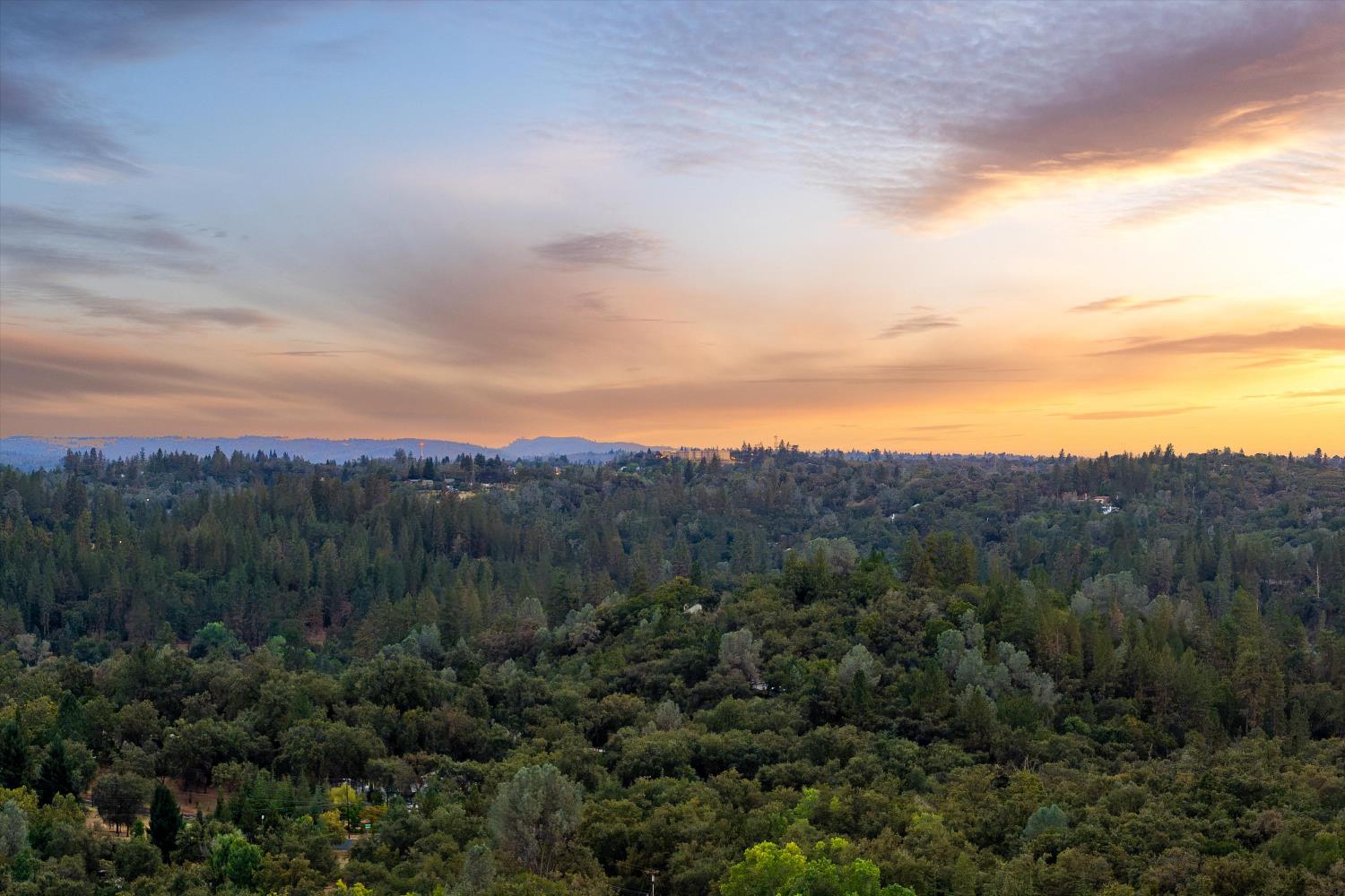 Wooded landscape and distant hills beneath a glowing sunset sky.