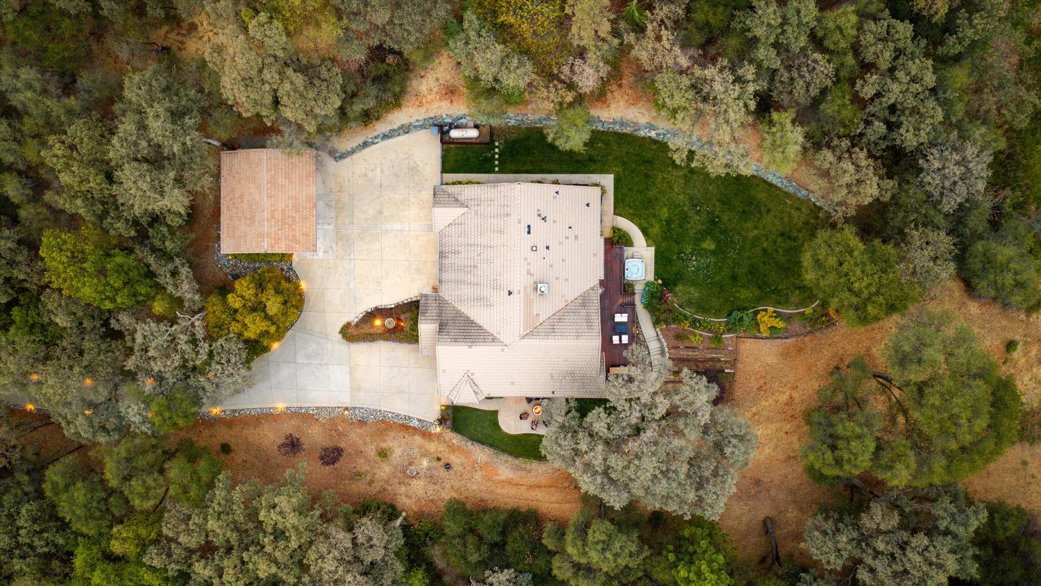 Aerial view of a tiled-roof home amid mature trees, with a curved driveway and backyard hot tub.