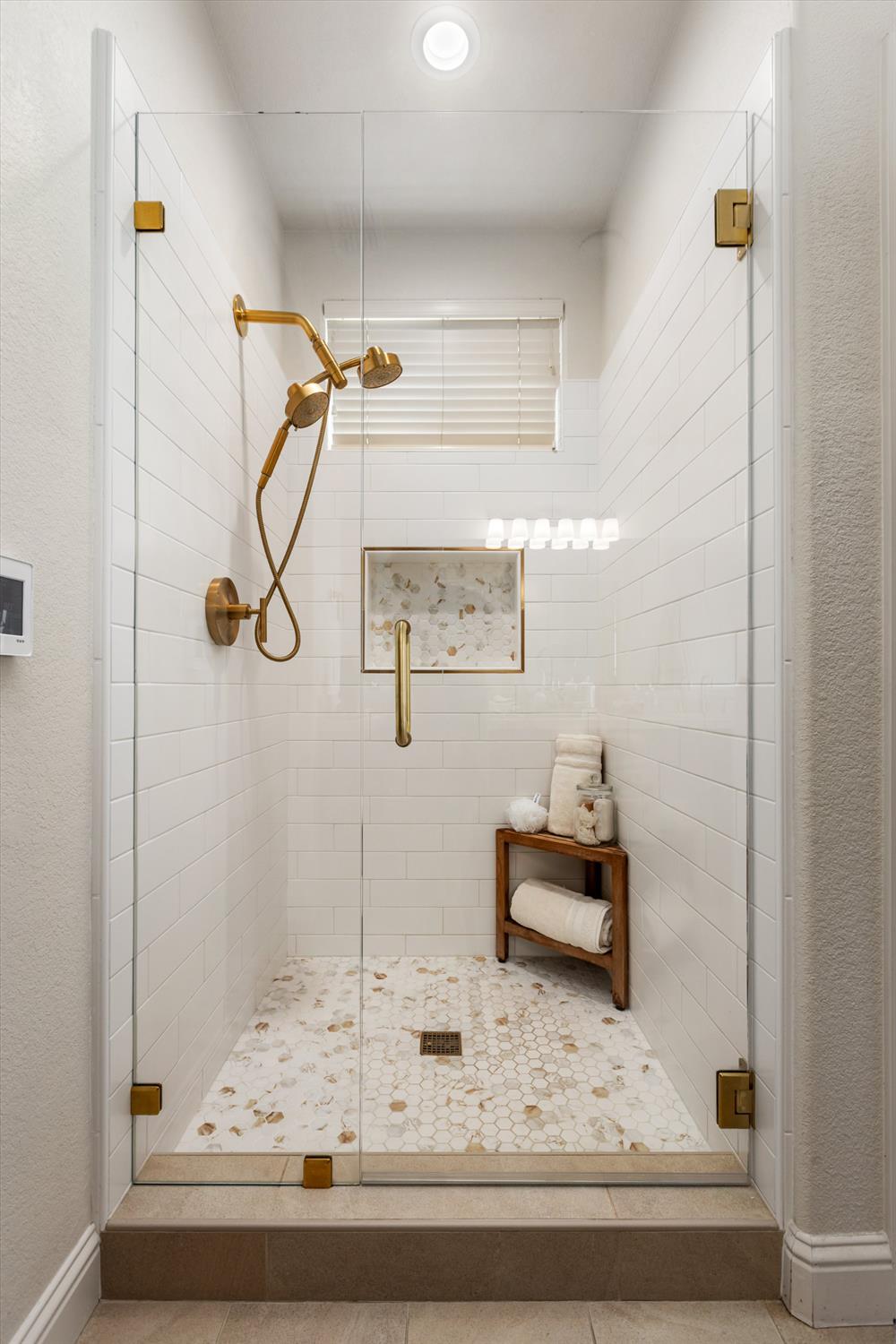 Walk-in shower with white tile, gold fixtures, patterned mosaic floor, and glass enclosure.