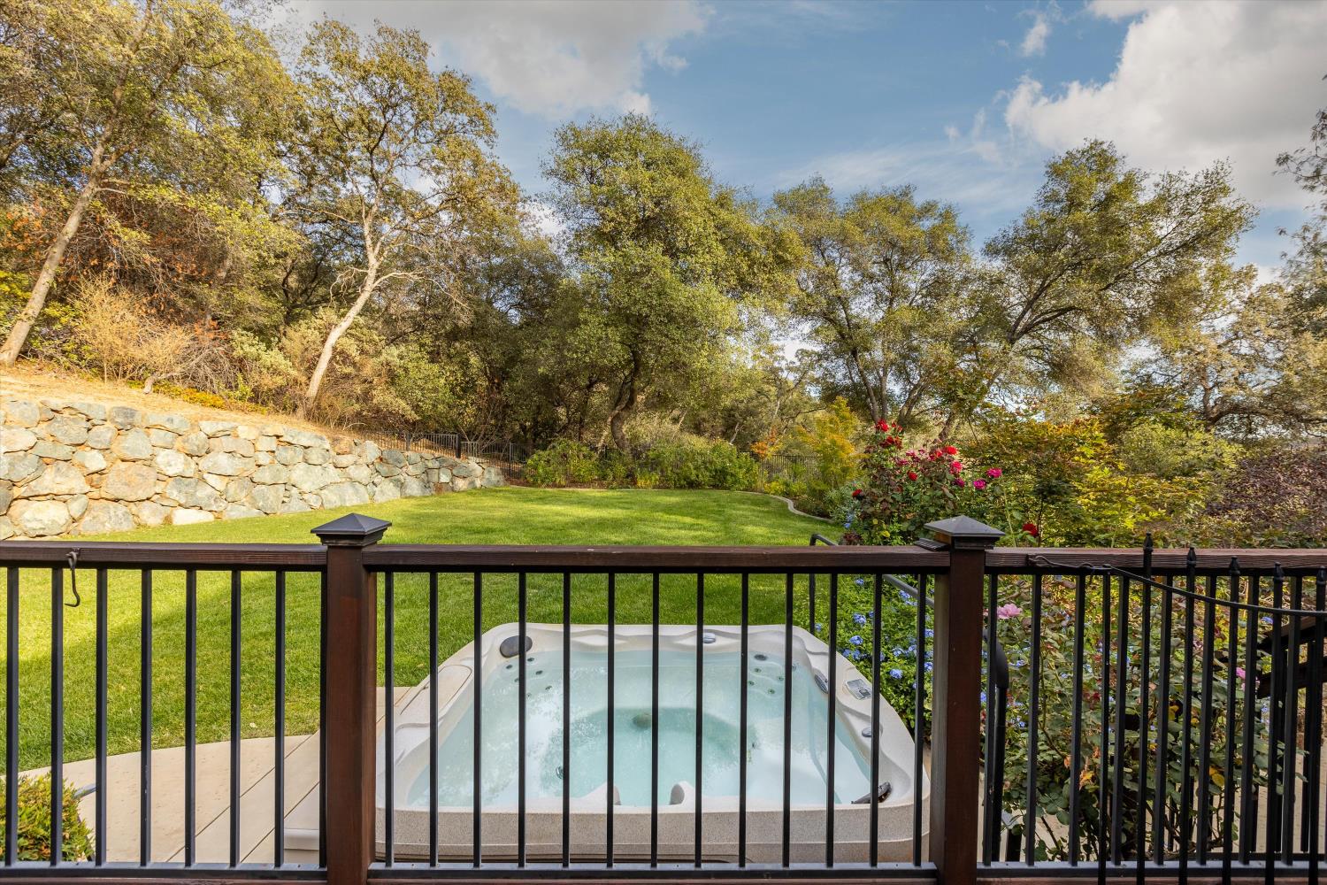 Backyard hot tub overlooking a lawn, stone retaining wall, and mature trees.
