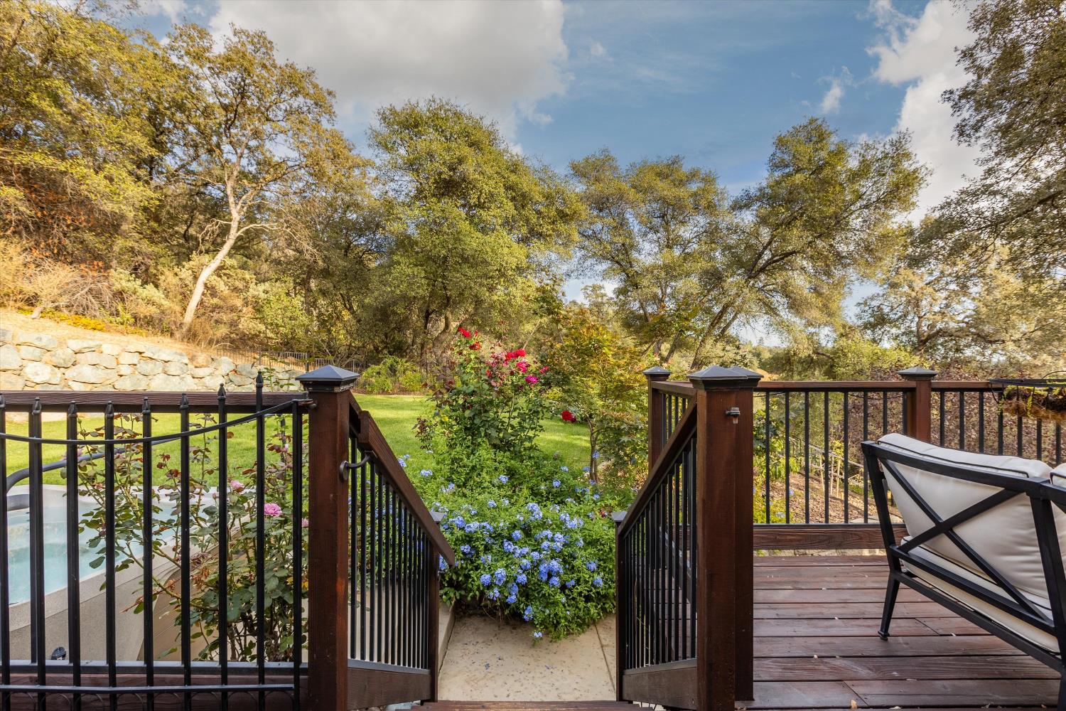 Wooden deck overlooks a flower-filled garden path, mature trees, and a glimpse of the pool.