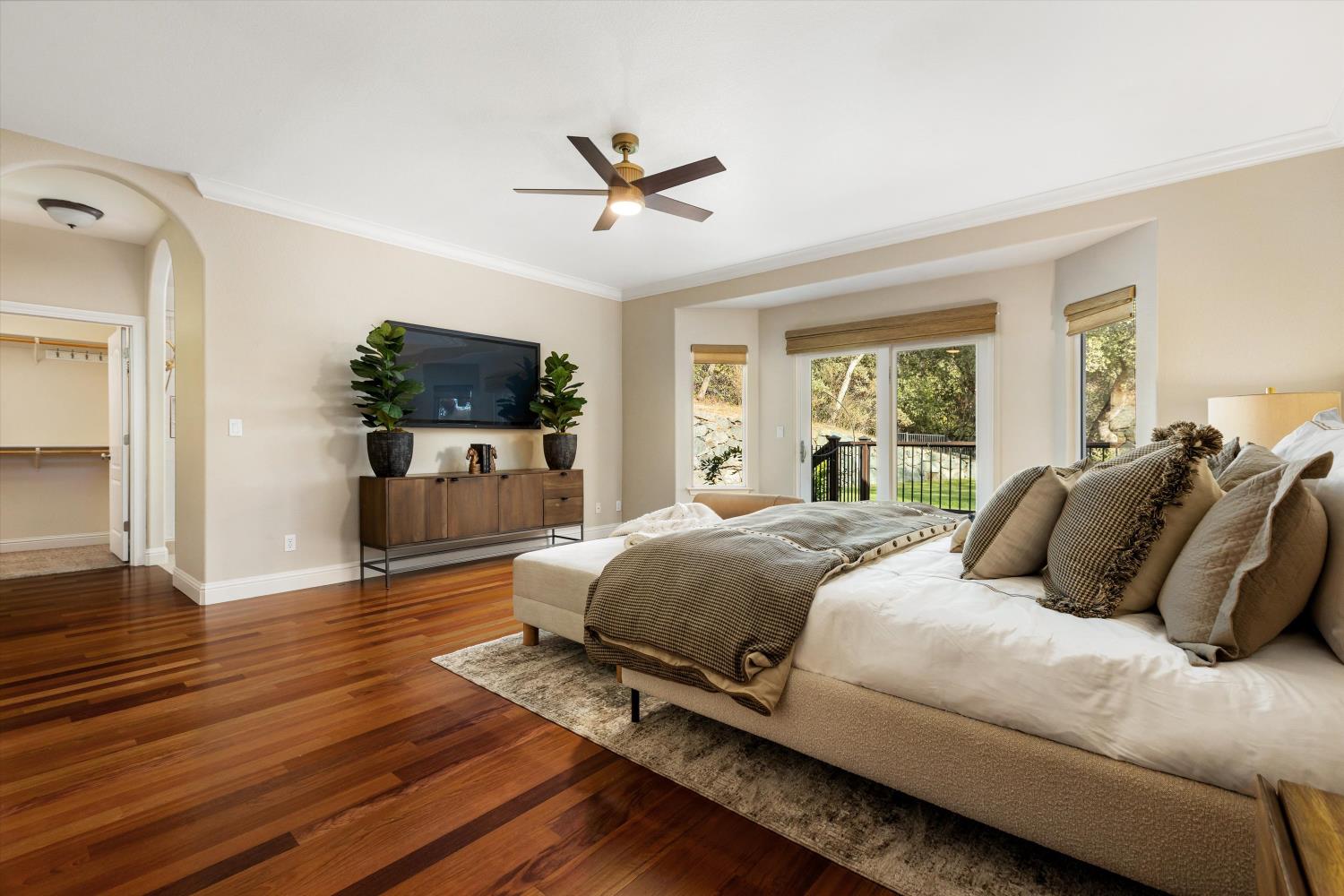 Staged bedroom with a large neutral-toned bed, hardwood floors, and sliding doors to a balcony.
