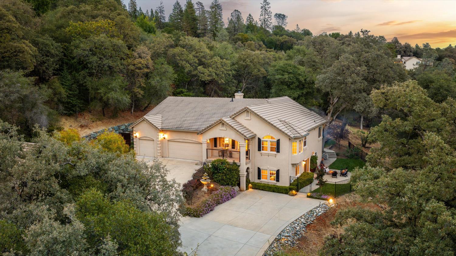 Aerial view of a two-story home nestled among trees, with a three-car garage and illuminated patio.