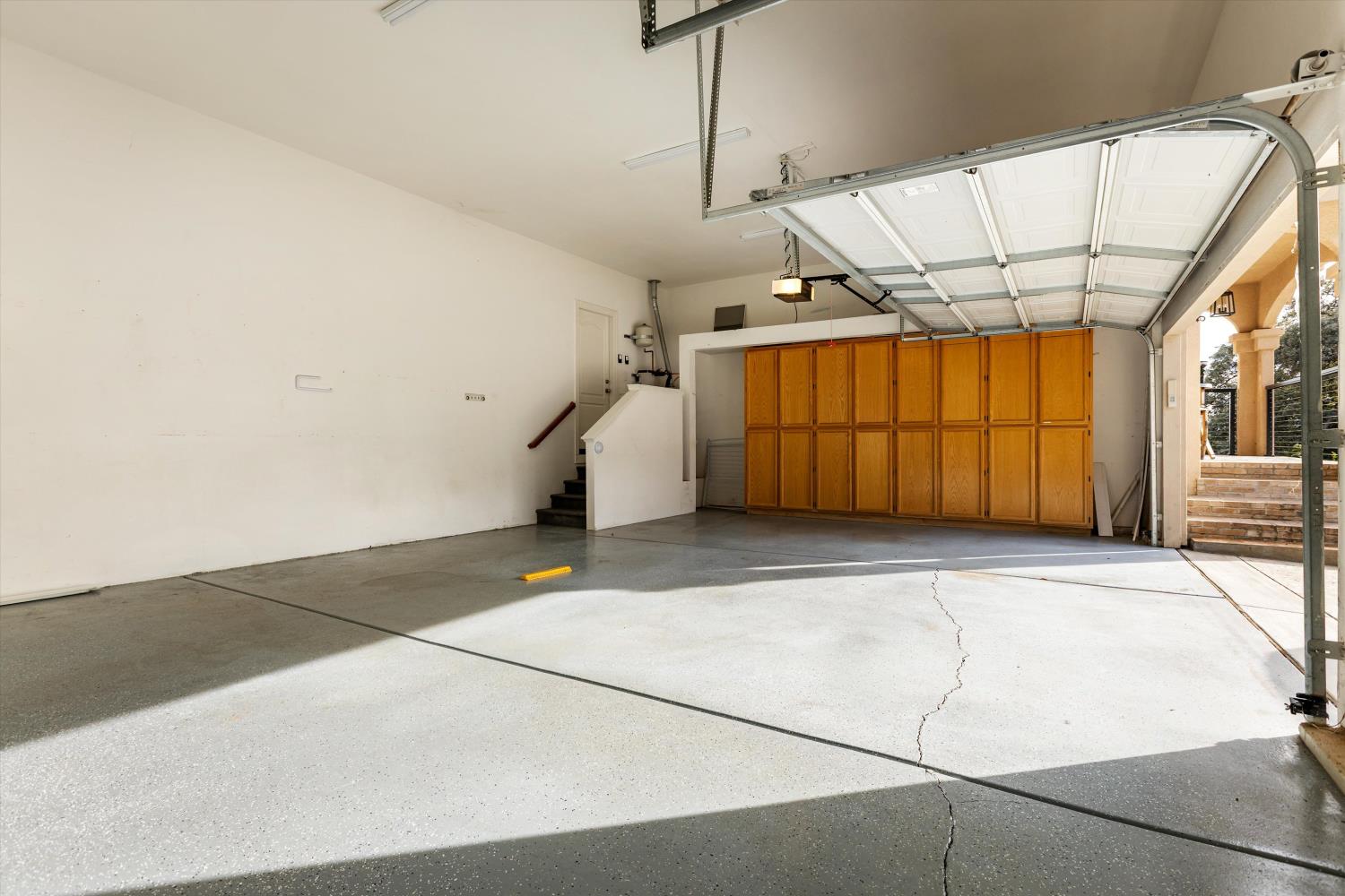 Garage with a raised overhead door, concrete floor, and a wall of wooden storage cabinets.