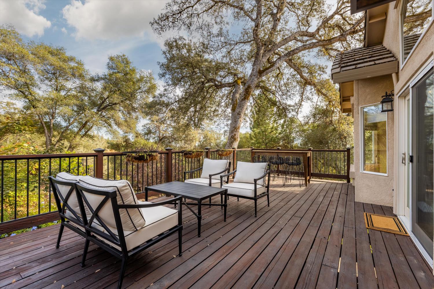 Elevated wooden deck with cushioned seating and dining area overlooking mature trees.