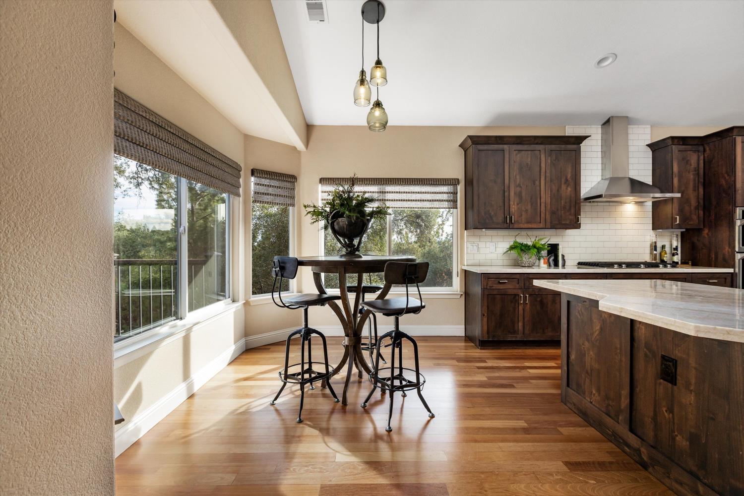 Kitchen with dark wood cabinetry, a white island, and a breakfast table beside large windows.