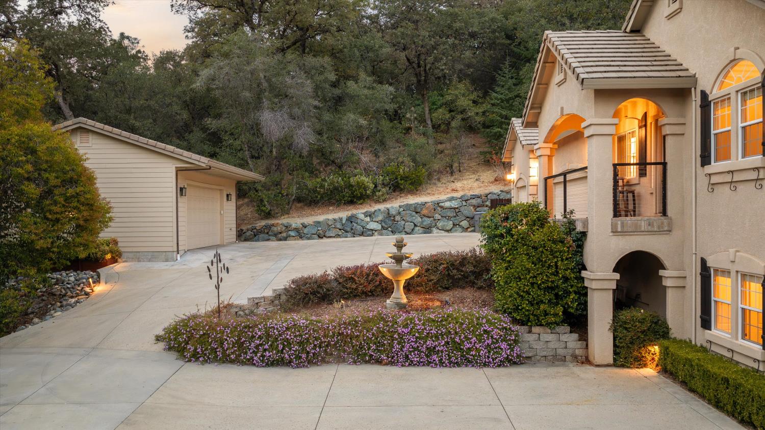 Home exterior at dusk with arched entryways, a courtyard fountain, and a detached garage.