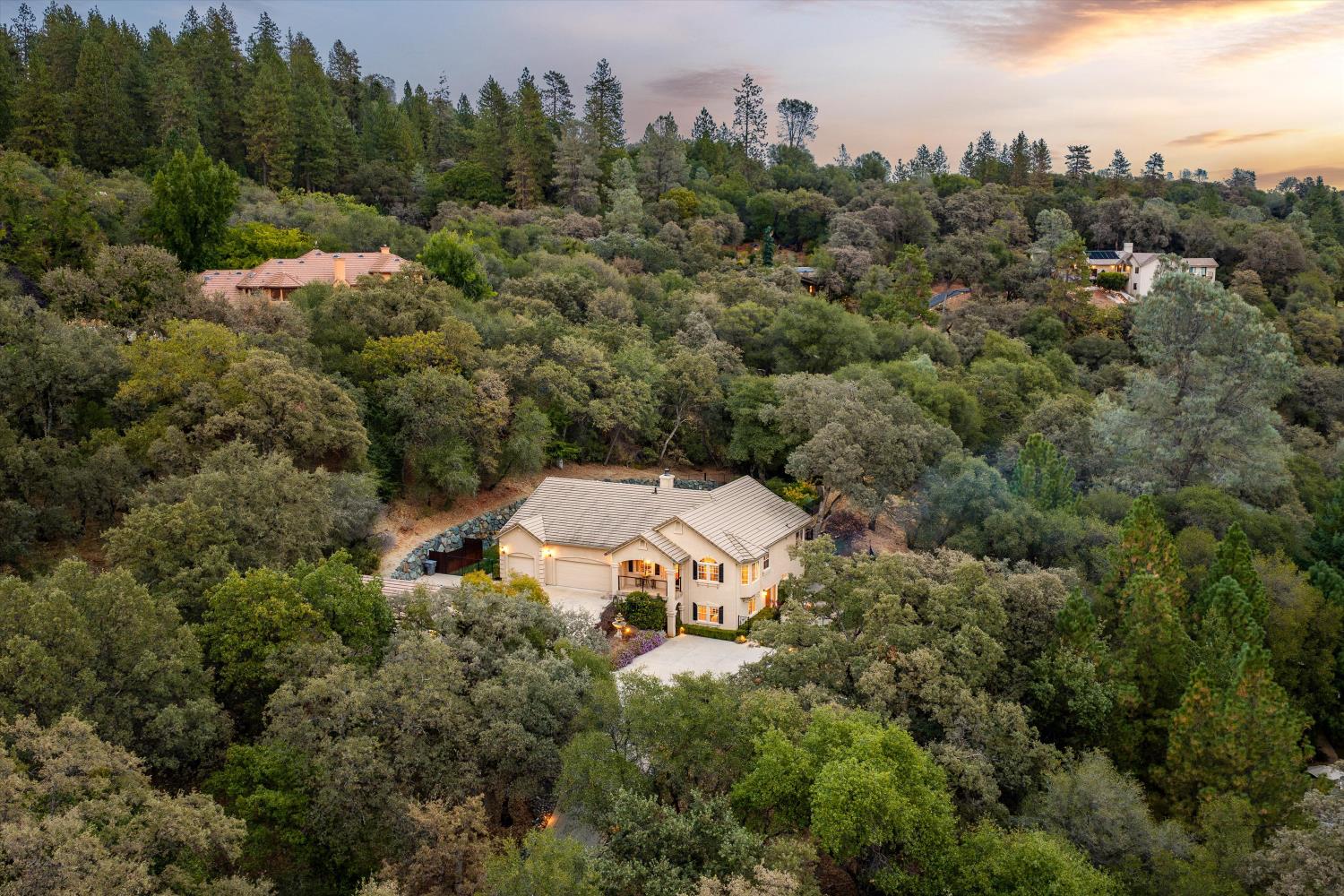 Aerial view of a two-story home nestled among dense trees at sunset.