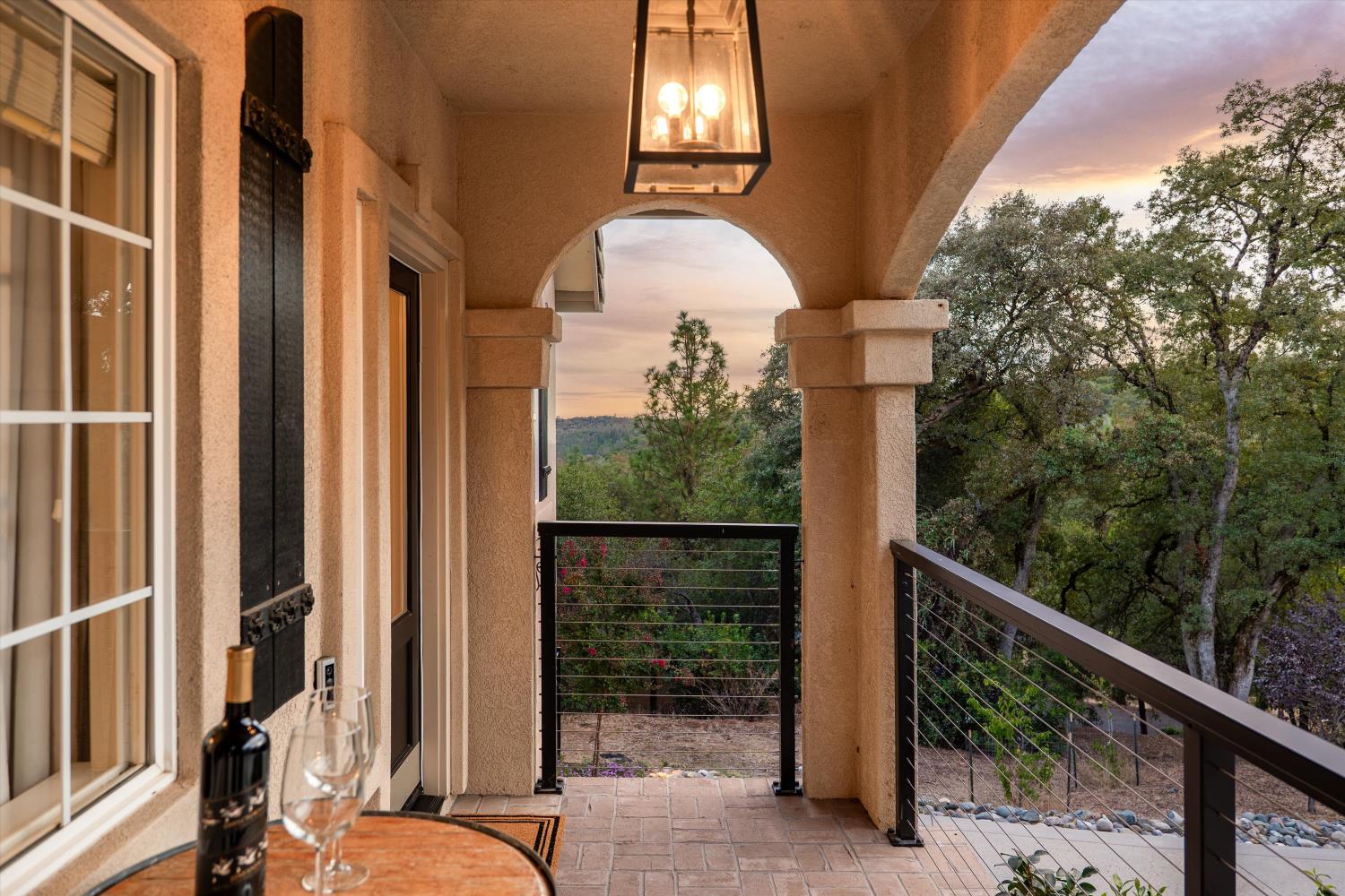 Covered arched porch overlooking trees at dusk, with tiled flooring and a table set with wine glasses.