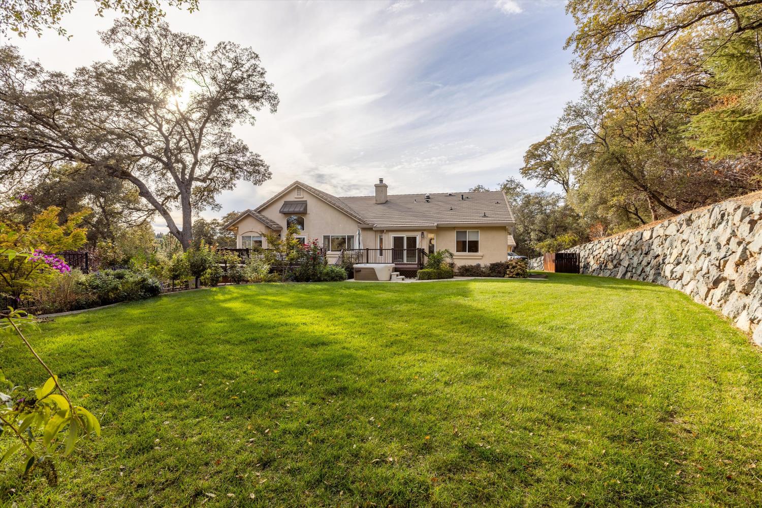 Home’s rear facade overlooking a broad lawn, with mature trees and a stone retaining wall.