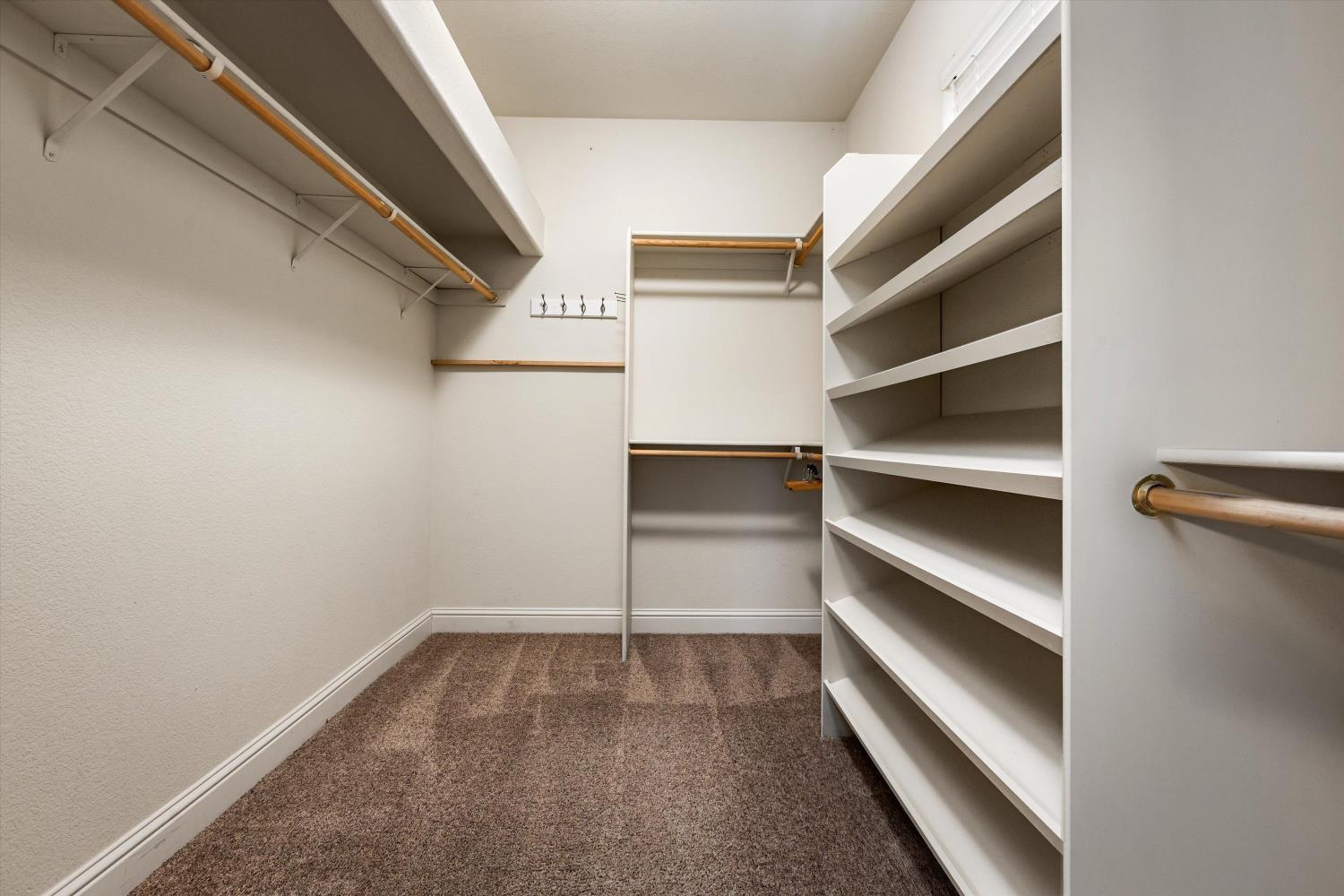 Walk-in closet with built-in shelving, wooden hanging rods, and brown carpet.