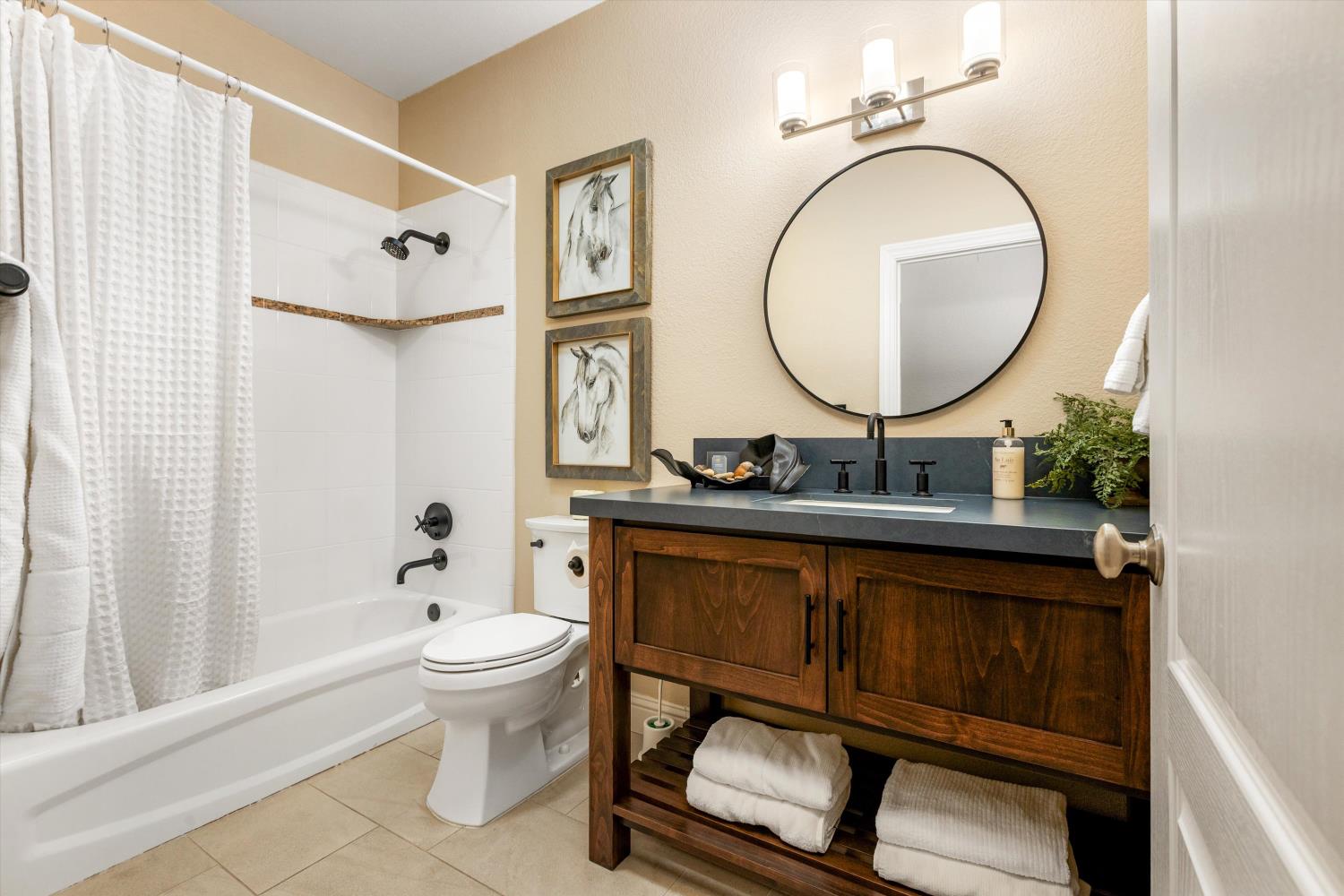 Bathroom with a dark wood vanity, round mirror, and white tub-shower.