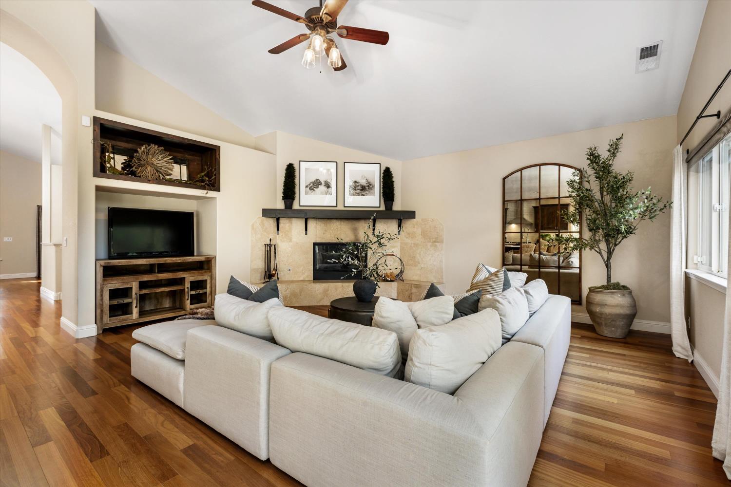 Living room with white sectional, stone fireplace, and warm hardwood floors.