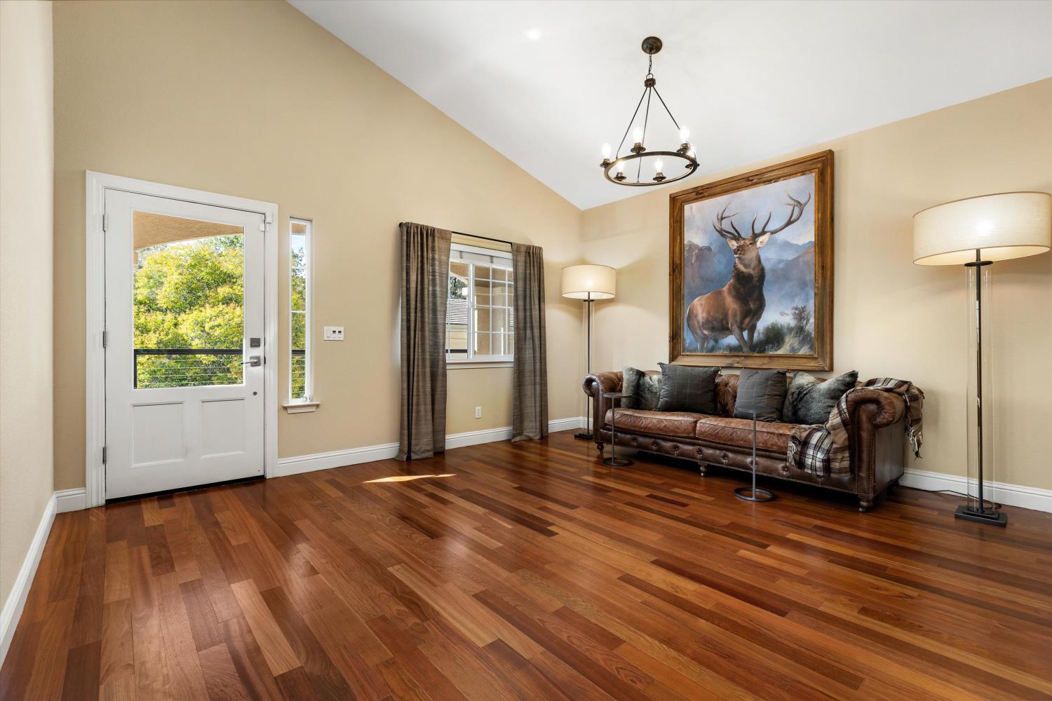Living room with vaulted ceiling, polished hardwood floors, and leather sofa beneath an elk painting.