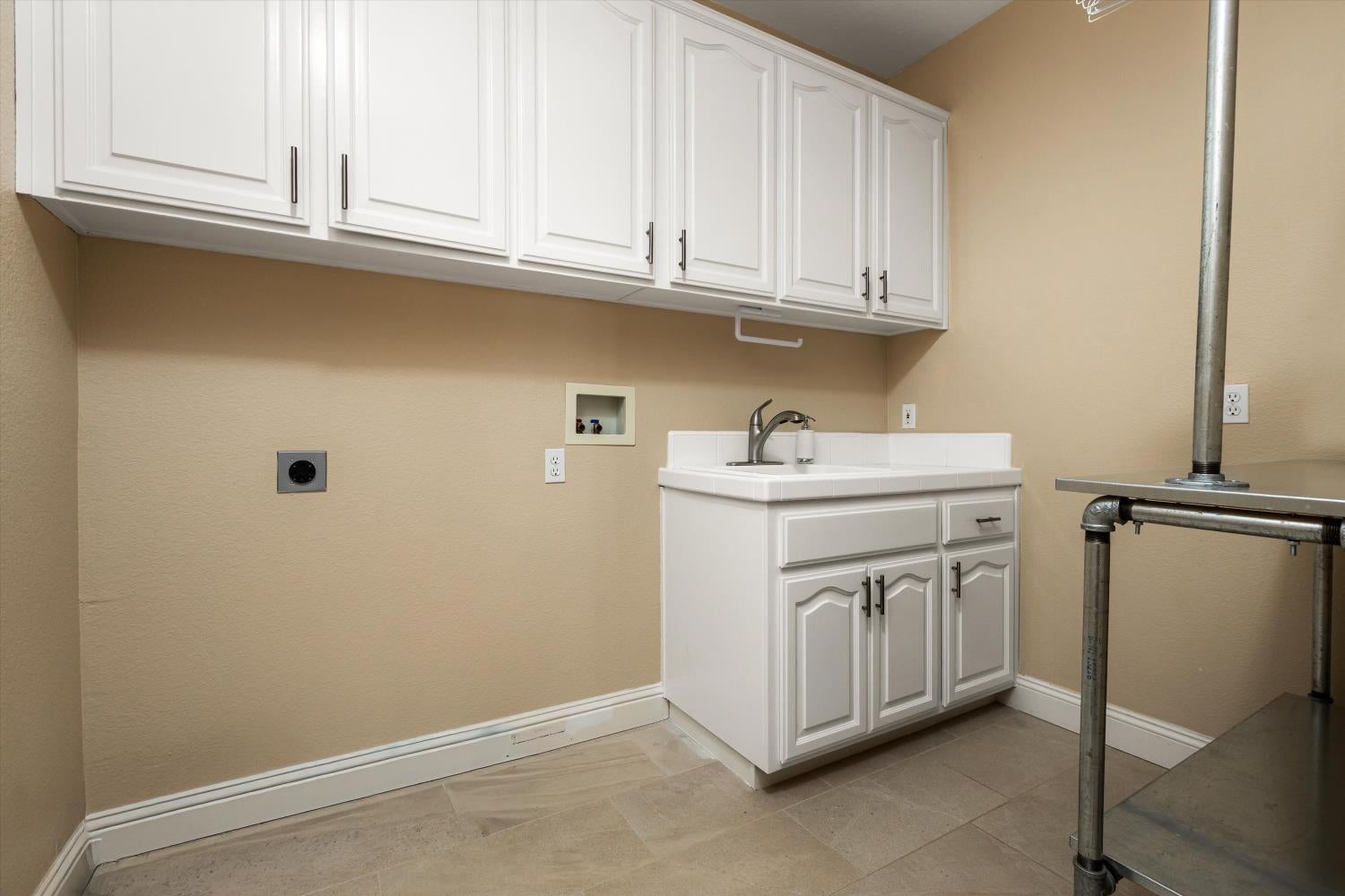 Laundry room with white cabinets and utility sink beside a metal rack.