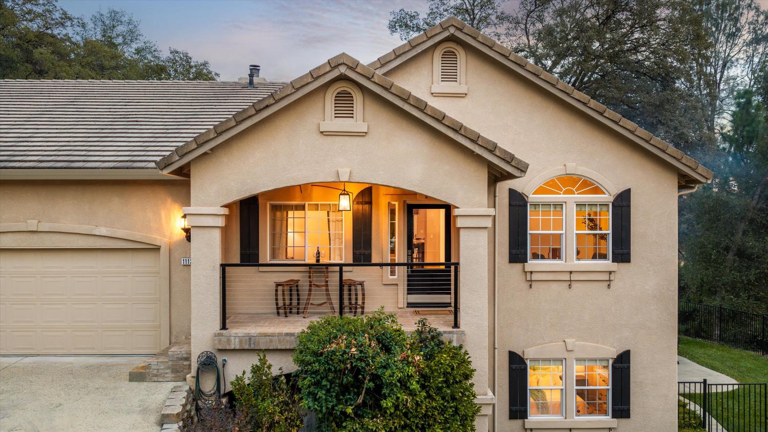 Two-story stucco home with a tiled roof, attached garage, and warmly lit covered balcony.