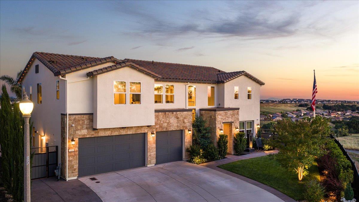 Two-story stucco home with stone accents and multiple garages at dusk.