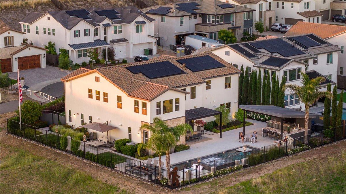 Aerial view of a two-story home with rooftop solar panels, a backyard pool, and a furnished patio.