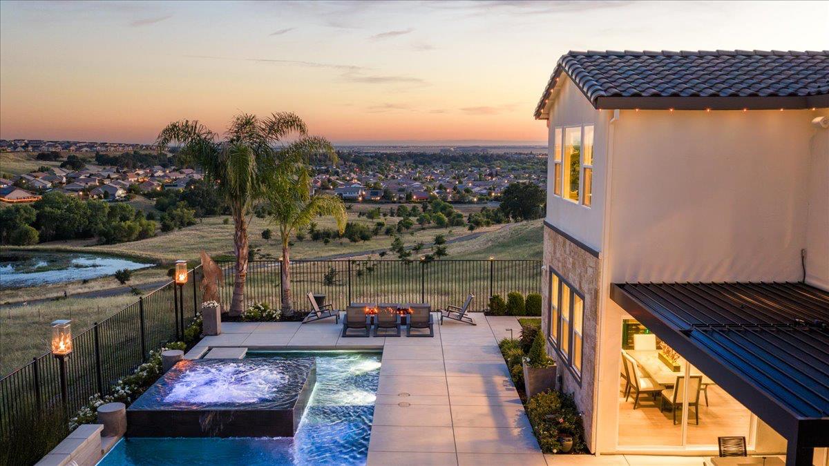 Modern home’s pool and raised spa overlook a suburban neighborhood at dusk.